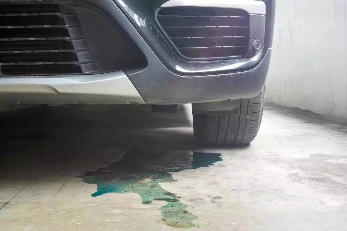 A puddle of blue colored liquid underneath the front of a Japanese car.