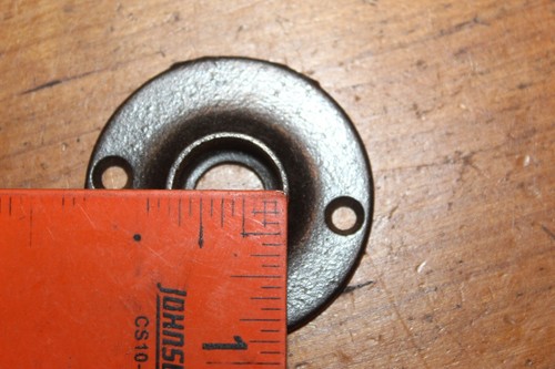 Round antique cast iron doorknob escutcheons with black text, shown beside a red measuring tape for scale.
