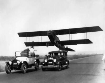 Vintage 1920s biplane flies over two classic cars as stuntmen atte- Old Photo