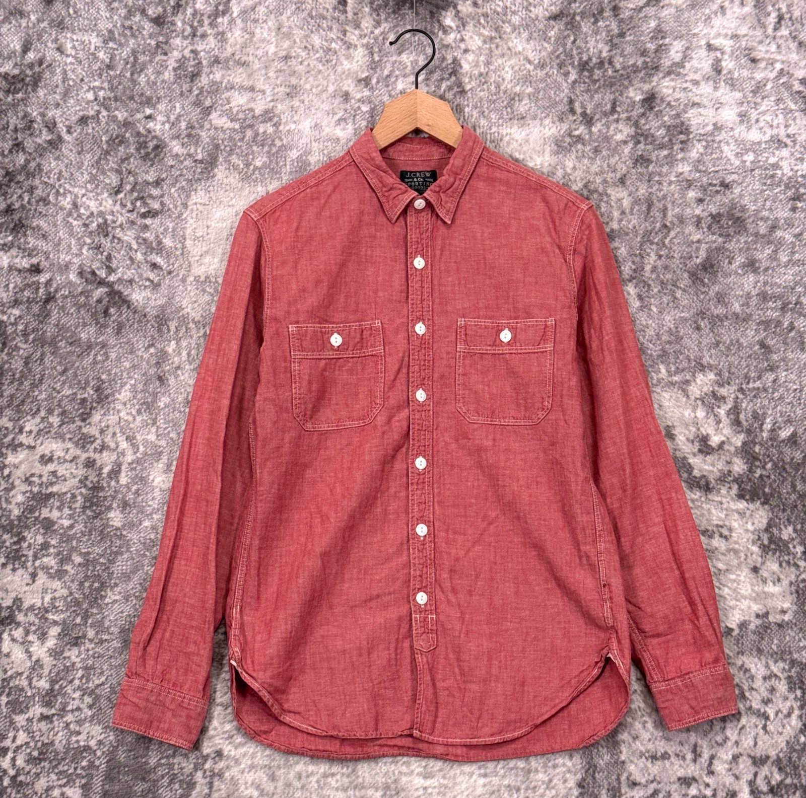 Red chambray button-up work shirt with two chest pockets, on a wooden hanger
