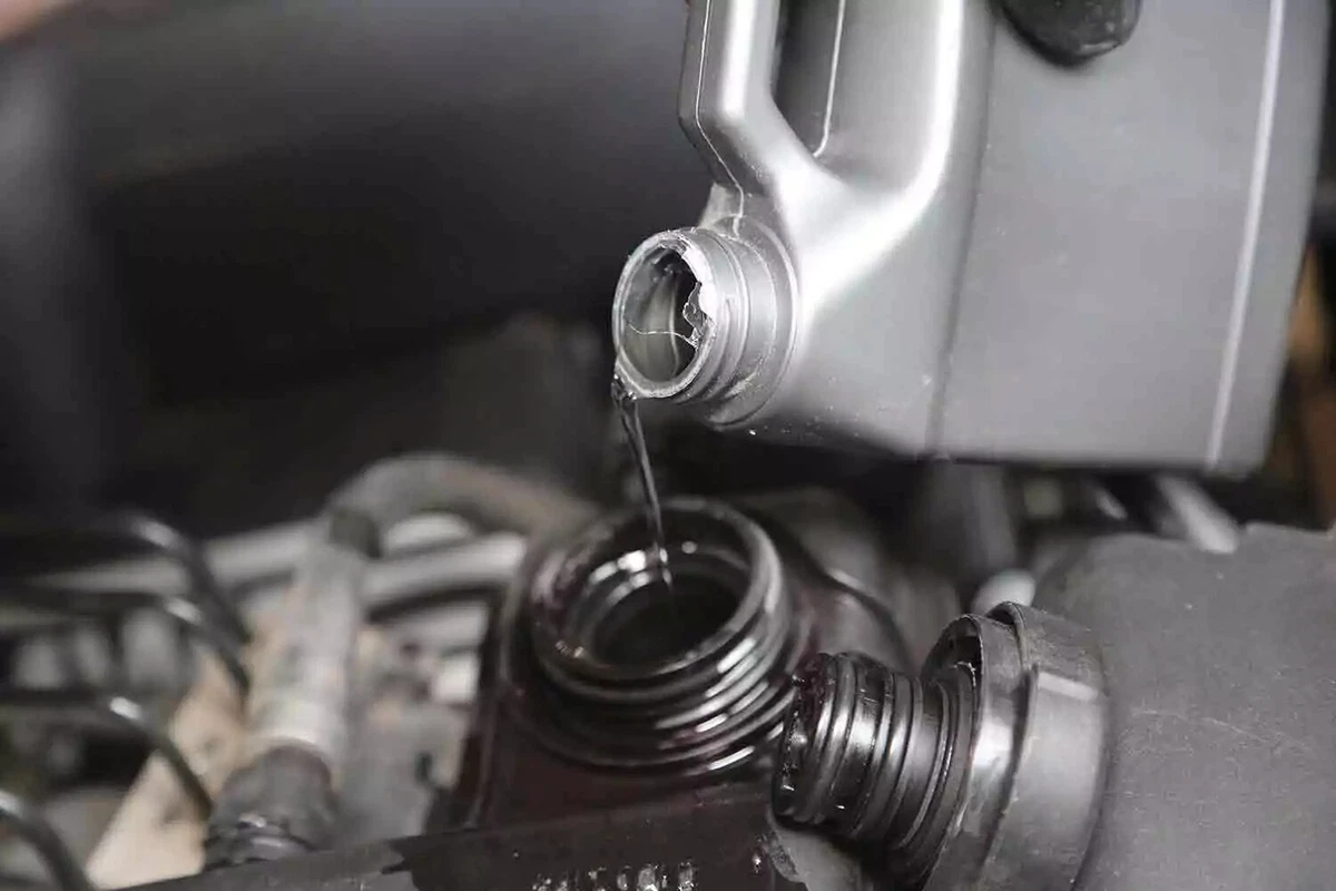 Cooling system flush is poured from a silver container into the coolant expansion reservoir of a vehicle.