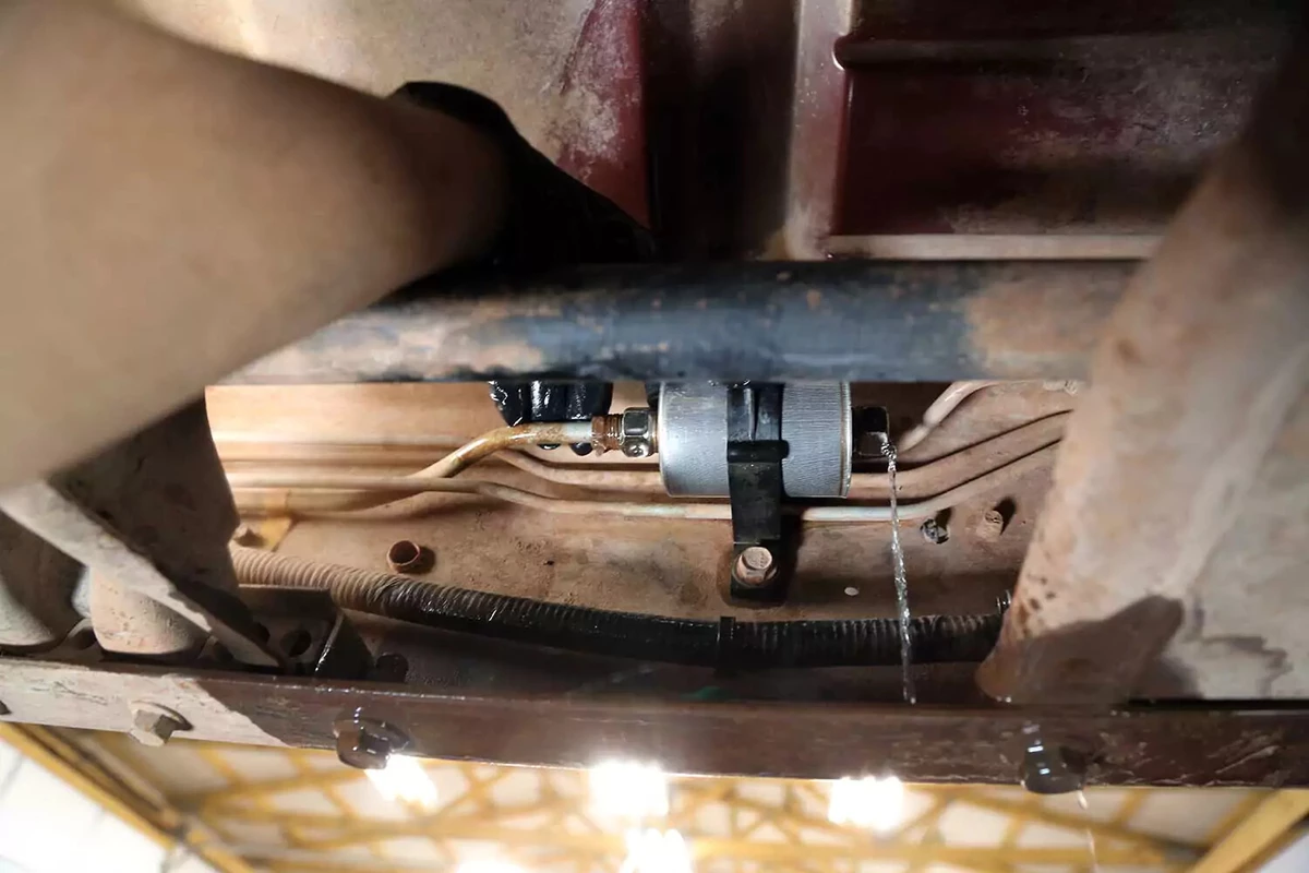 A mechanic installs the fuel tank line on the filter as fuel drains out the open fitting.