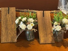 Ball jar that holds fairy lights and flowers hangs on wood like backing board