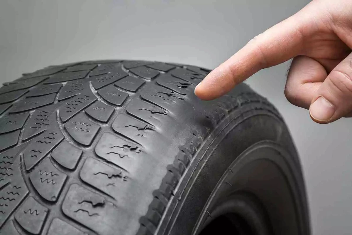 A hand pointing to uneven wear on a tire.