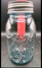 Clear vintage glass mason jar with embossed “Ball” logo, zinc lid, and red-colored liquid inside.