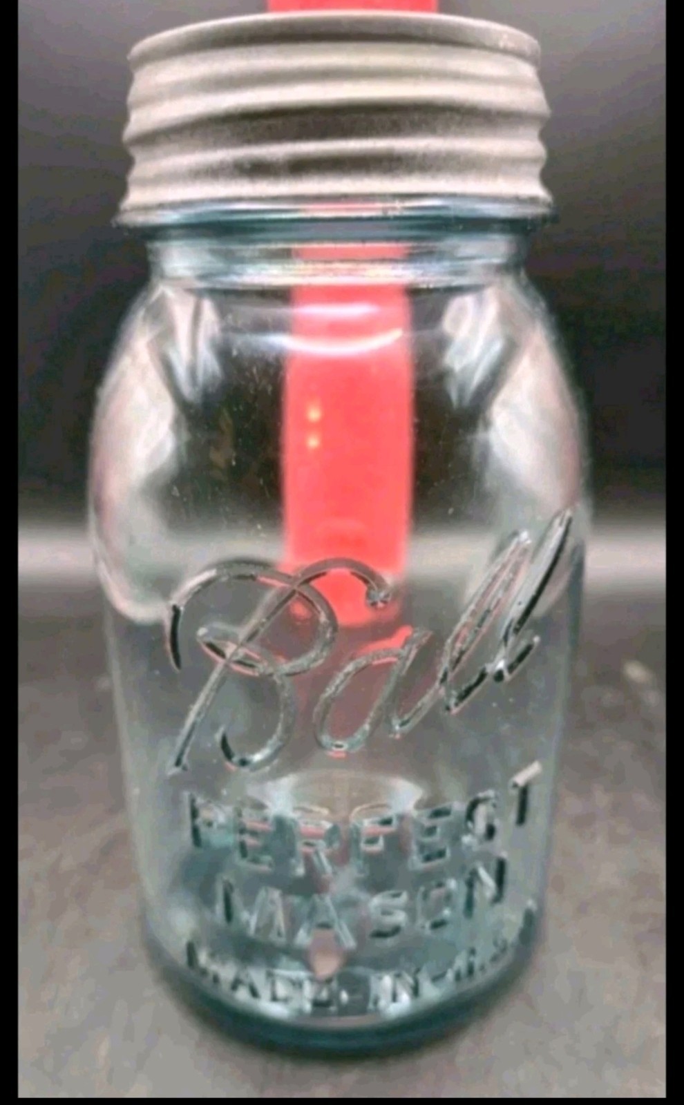 Clear vintage glass mason jar with embossed “Ball” logo, zinc lid, and red-colored liquid inside.