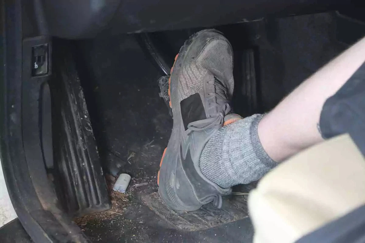 A mechanic’s assistant wearing shorts and sneakers presses the brake pedal in an older vehicle to check for issues.