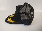Black trucker hat with yellow National Rifle Association logo and text, snapback style, mesh front panel, and black brim.
