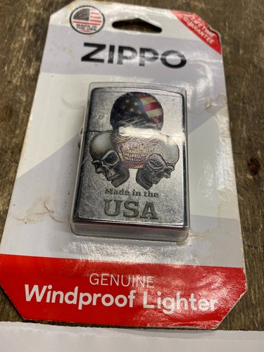 Silver Zippo lighter with three skulls, US flag, and red “Made in U.S.A.” text on white box.