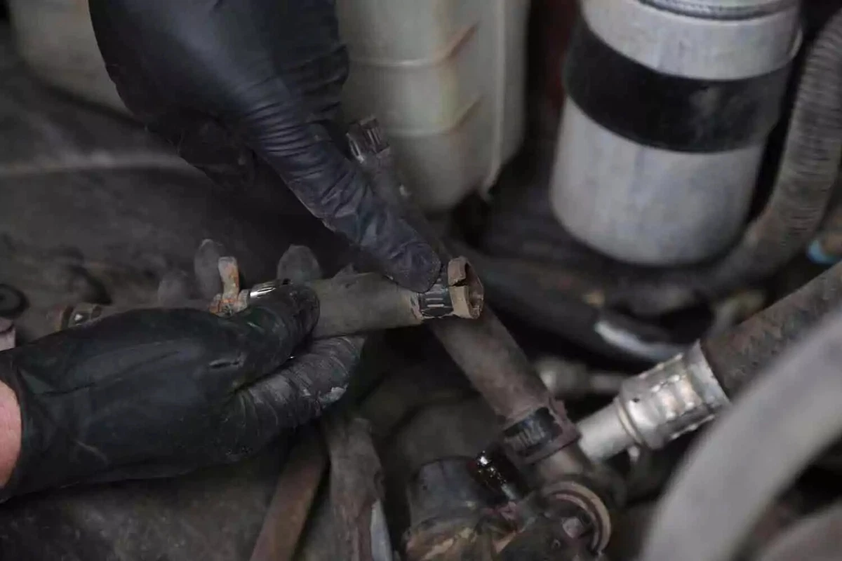 A mechanic wearing black gloves holds the old heater core hose.