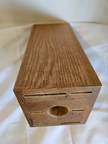Rectangular solid honey oak wood knife storage block with 13 slots and a central circular hole on a white fabric surface.