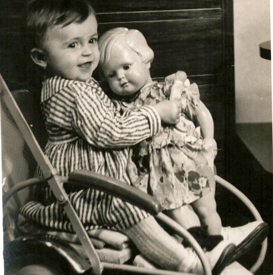 A genuine vintage snapshot of a toddler posed with an enormous, unsettling doll in a buggy — peak outsider art energy and instant conversation starter.