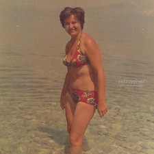 Attraente donna in bikini rosso floreale in piedi in mare trasparente foto d'...