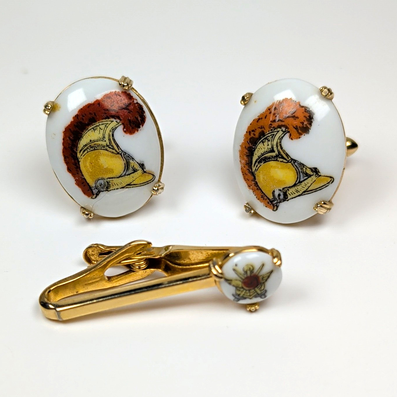Gold-tone cufflinks and tie clip set with Roman helmet motif on a white background.