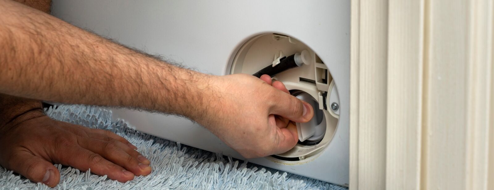 Jemand öffnet die Klappe der Bodenwanne einer Miele-Waschmaschine.