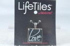 Silver metal pendant with square glass tile displaying white “LOVE” text, hanging from black card labeled “Life Tiles.”