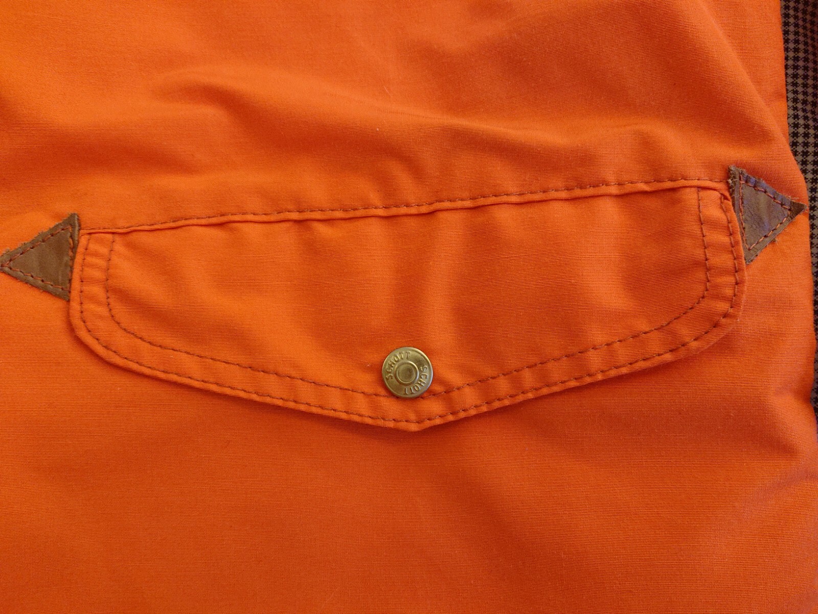 Orange cotton-nylon Perfecto parka with front snap pocket, flap pockets, and triangular stitched accents.