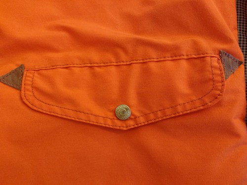 Orange cotton-nylon Perfecto parka with front snap pocket, flap pockets, and triangular stitched accents.