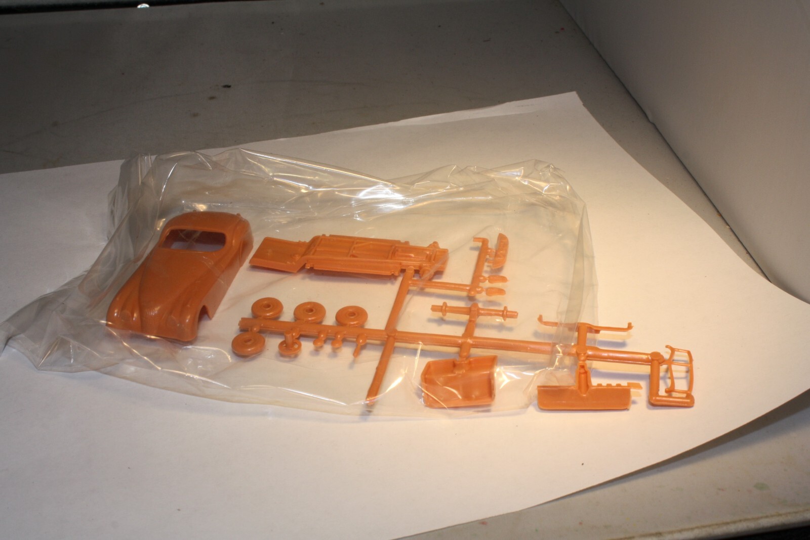 Clear plastic bag containing 1950s Ferrari & Jaguar XK120 roadster parts—orange body, seats, and accessories.