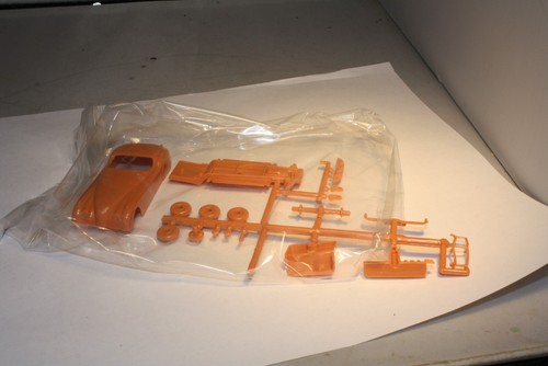 Clear plastic bag containing 1950s Ferrari & Jaguar XK120 roadster parts—orange body, seats, and accessories.