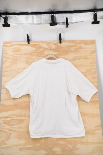 White vintage Harley-Davidson Sturgis 2002 men’s 2XL polo shirt hanging on a black hanger against a light wood background.