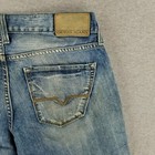 Back view of vintage blue GUESS jeans with asymmetrical button fly, tan leather patch, and visible wear marks on fabric.