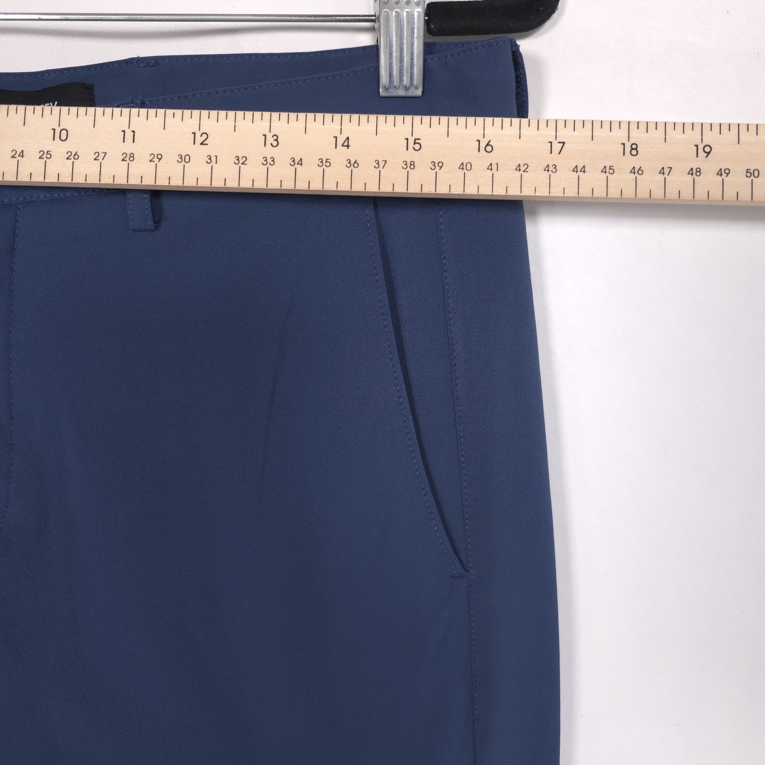 Blue 32 slim-fit THEORY men’s dress pants with front button closure, belt loops, and straight hem, hanging on wooden ruler.