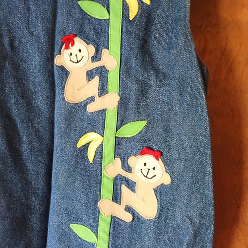 Blue denim kids’ 2-piece outfit with embroidered monkeys climbing green leaves, red headscarf, and yellow banana accents.