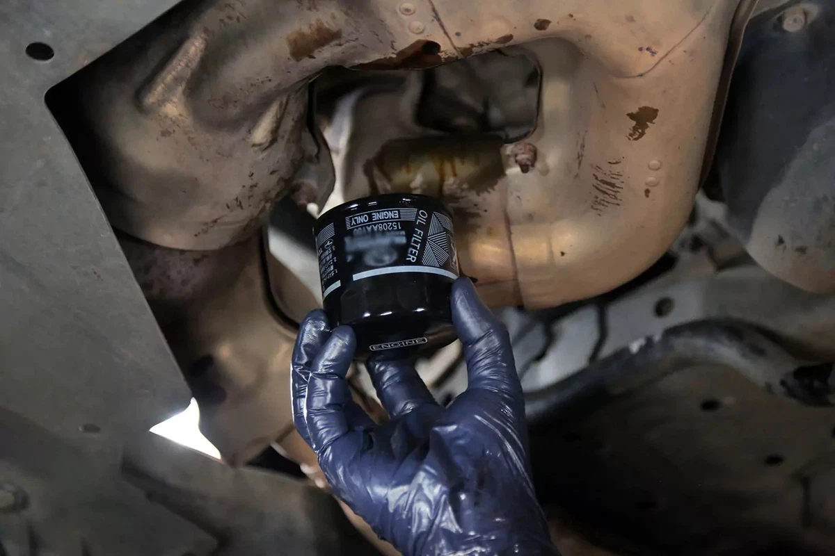 A mechanic reaches under an engine to install an engine filter.