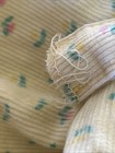 Close-up of worn white corduroy fabric with small colorful floral print and a loose white sewing seam.
