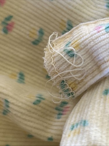Close-up of worn white corduroy fabric with small colorful floral print and a loose white sewing seam.
