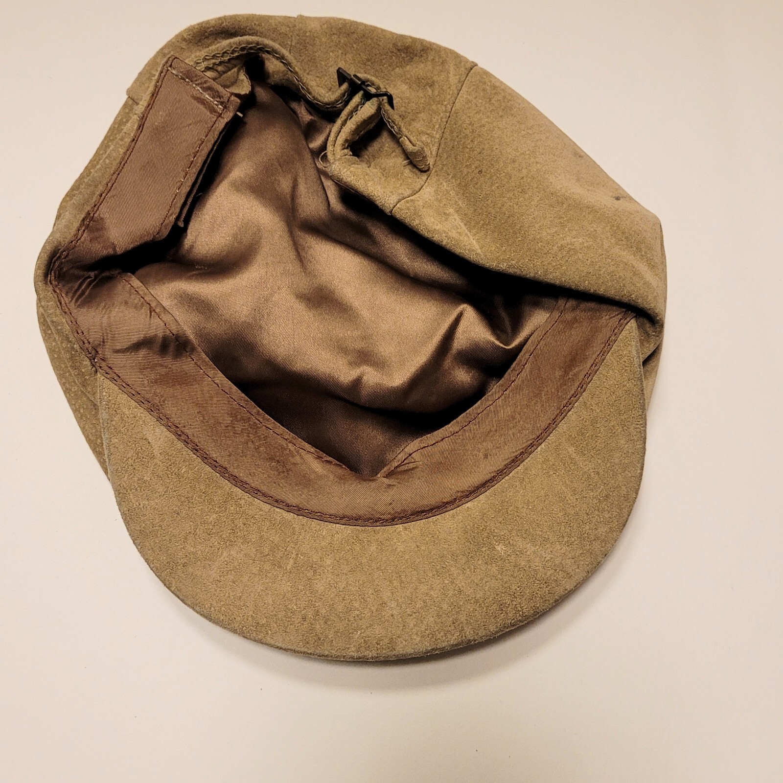 Tan suede leather newsboy cap with unbranded fabric interior, long ears, and adjustable strap.