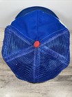 Blue and white snapback trucker hat with gold stitching and red button, shown from the back on a wooden surface.