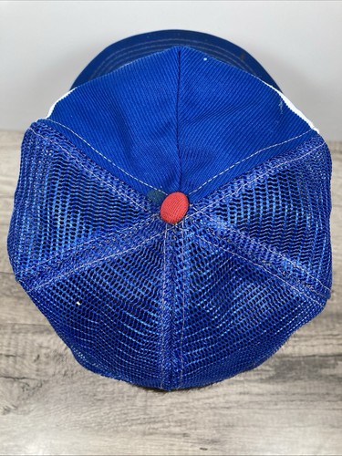 Blue and white snapback trucker hat with gold stitching and red button, shown from the back on a wooden surface.