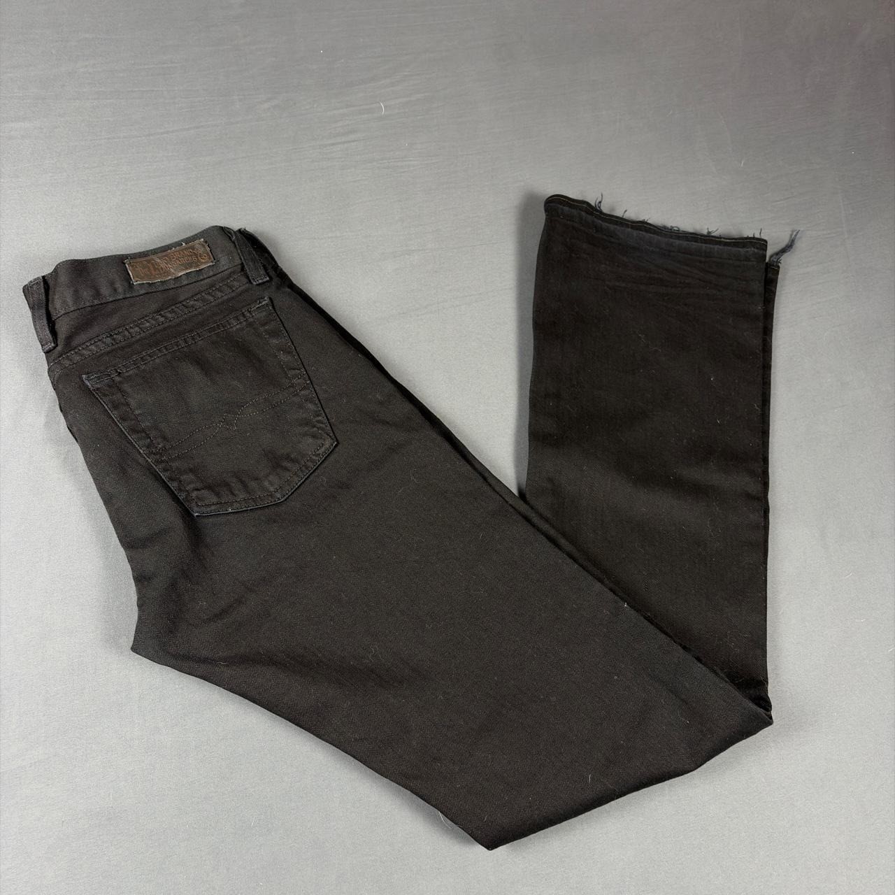 Black faded bootcut jeans with back pocket and brown leather patch on waistband, folded on light gray surface.