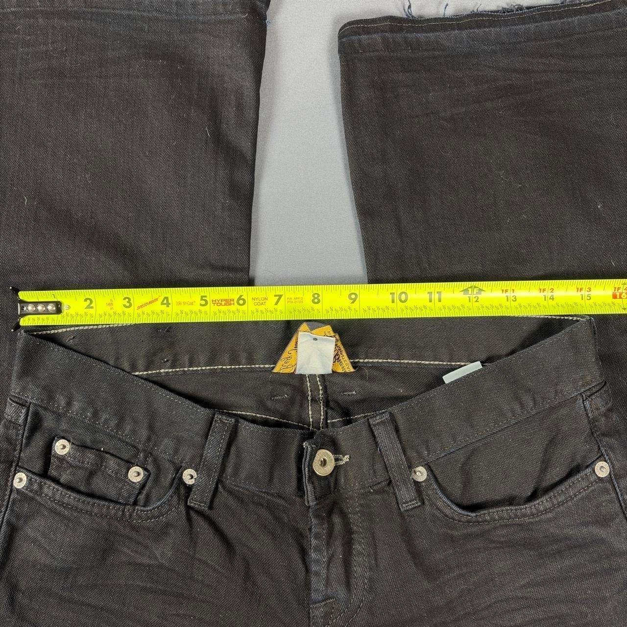 Black faded bootcut jeans with white stitching, front pockets, and visible yellow measuring tape across the waistband.