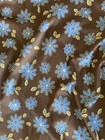 Brown fabric with blue and yellow flower print, green leaves, USA Made label at bottom.