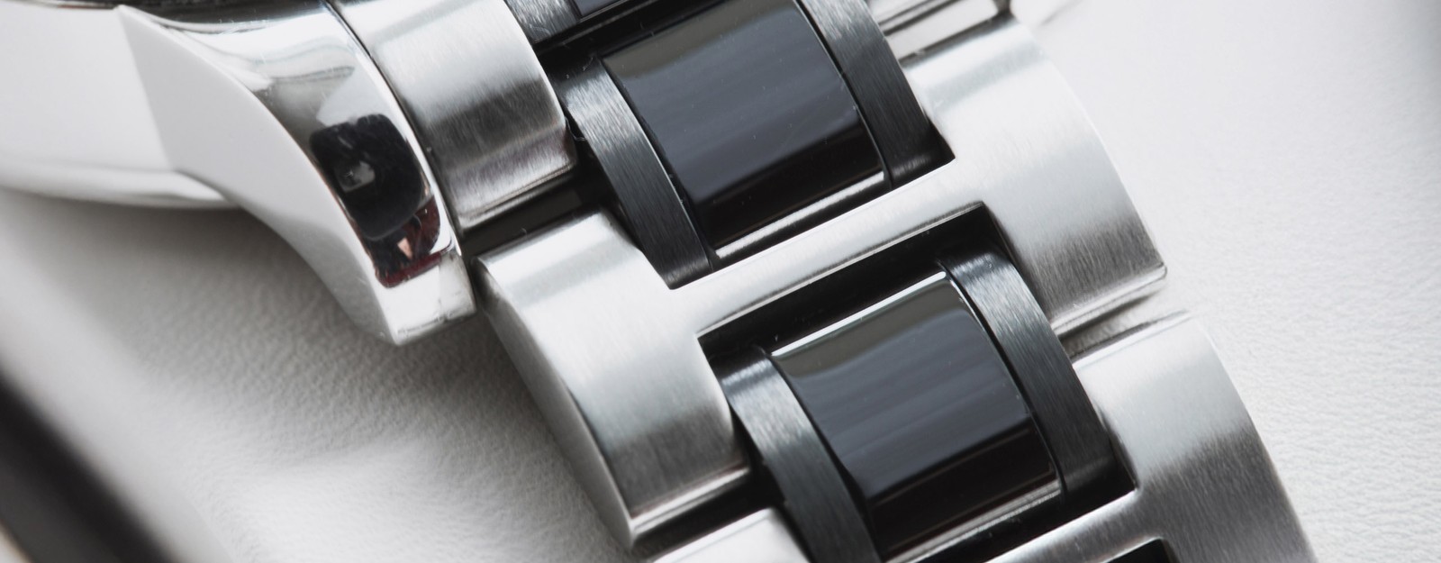 Detailaufnahme eines Uhrenarmbands, bestehend aus Gliedern aus gebürstetem Edelstahl im Wechsel mit schwarzen Einsätzen.