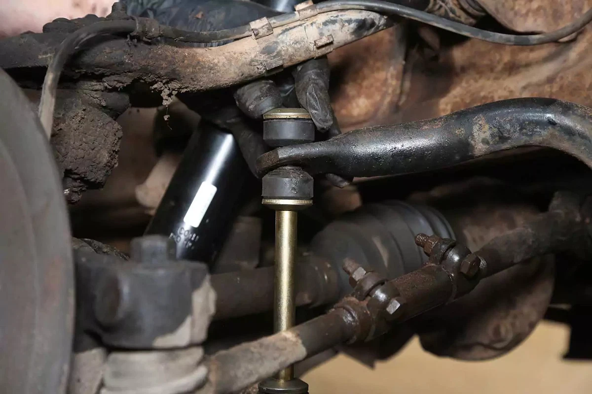 A mechanic drops the top bushing and washer onto the bolt prior to pushing the nipple into the sway bar hole.