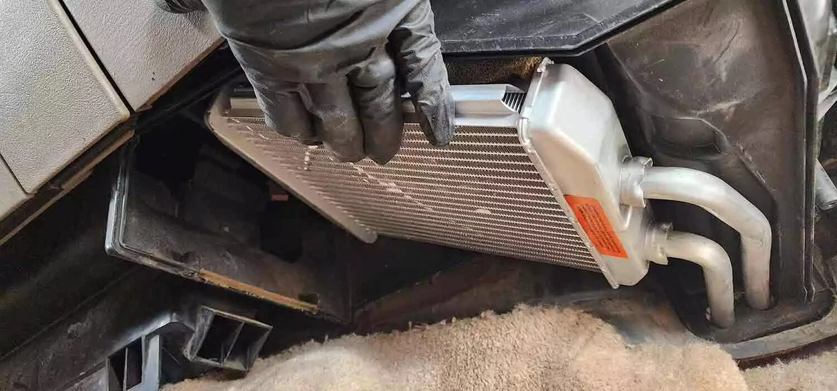 A mechanic wearing a black glove positions the new heater core inside the HVAC box.