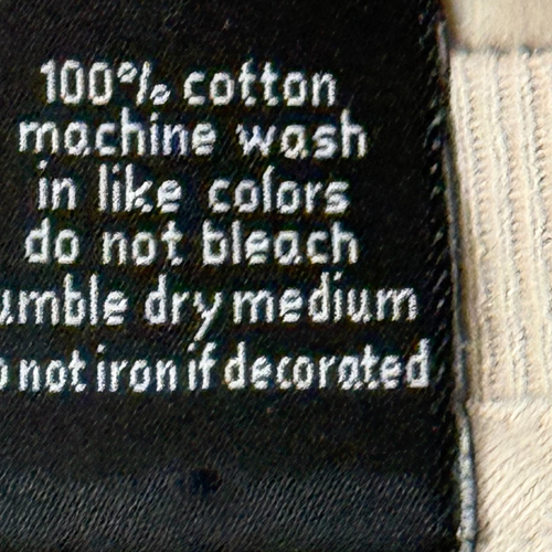 White printed inner label of Y2K VTG T&C surf shirt with black text, laundry instructions, and yellow floral accents.
