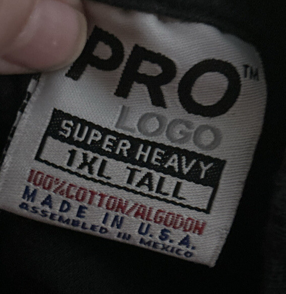 White fabric tag on black shirt with red “PRO LOGO” text, black “1XL Tall” label, and blue “Made in U.S.A.”