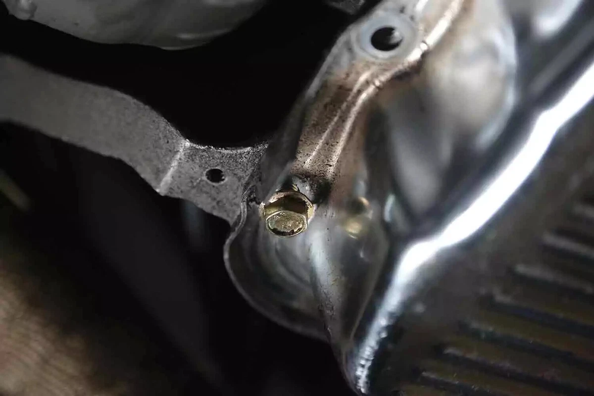 One of the 2 remaining bolts of a vehicle's transmission pan after being loosened.