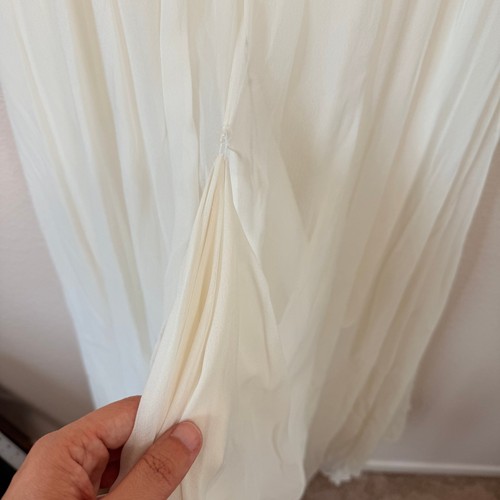 Hand touching the side seam of a white silk wedding dress with ruched front and sweetheart neckline, made in USA.