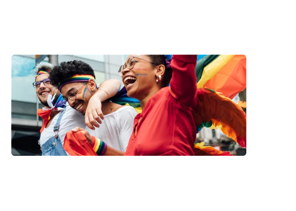 Drei Menschen mit Regenbogenschminke und Bändern liegen sich in den Armen und feiern. Sie sind glücklich.