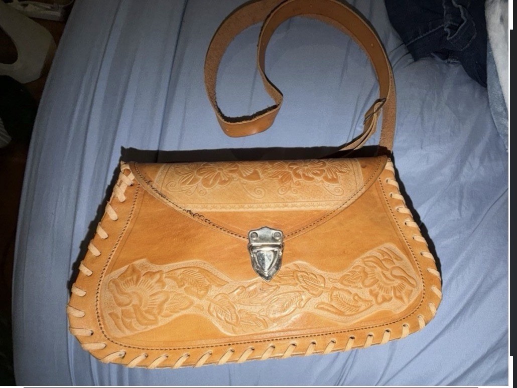 Tan hand-tooled floral leather saddle bag with whipstitched edges.