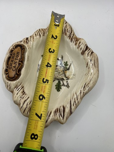 Brown ceramic sink with carved Grand Canyon owl and green leaf design, shown on white background with measuring tape.
