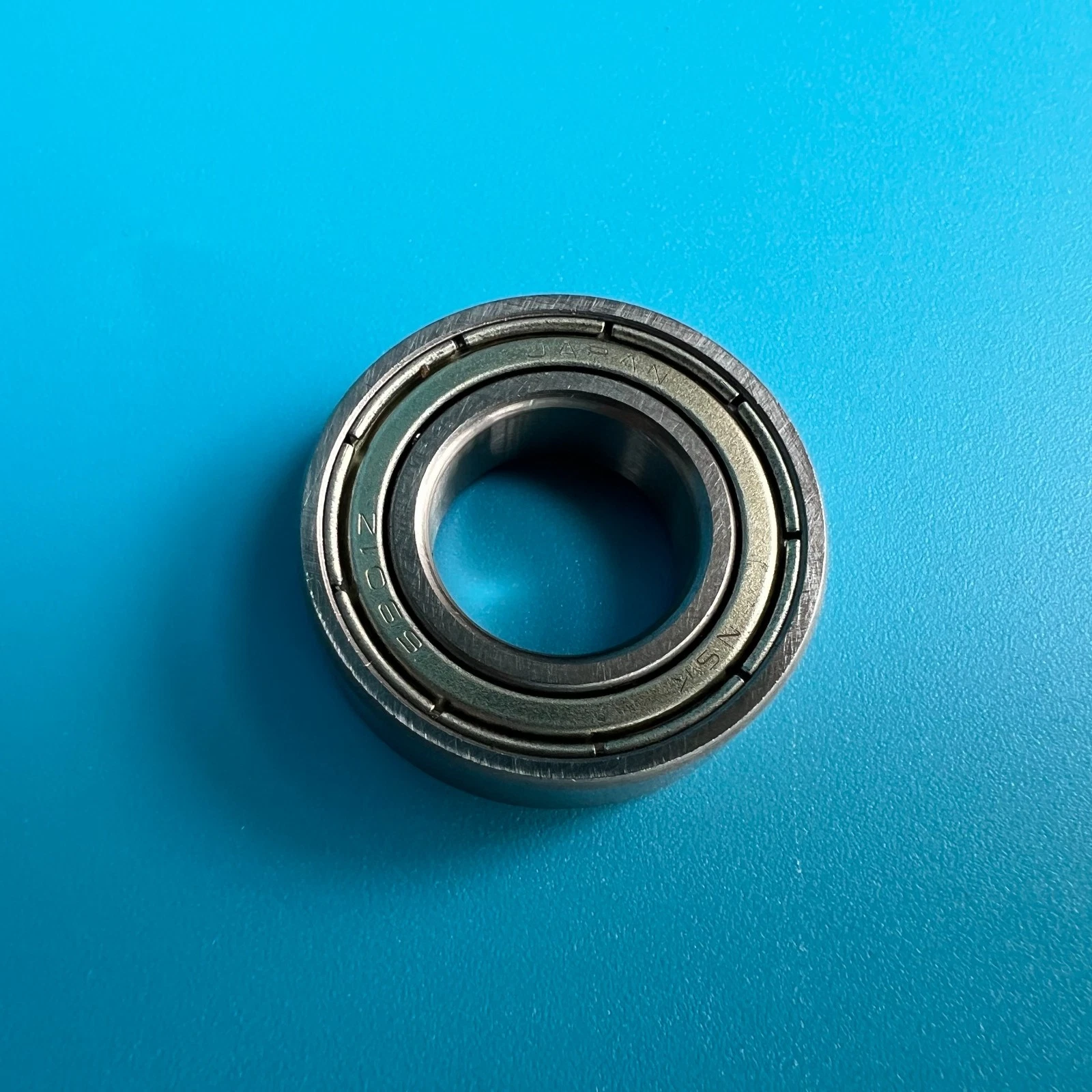 Metal H001059 bearing with visible screw hole, marked “NORITSU QSS 32/34/37/38” on blue background.