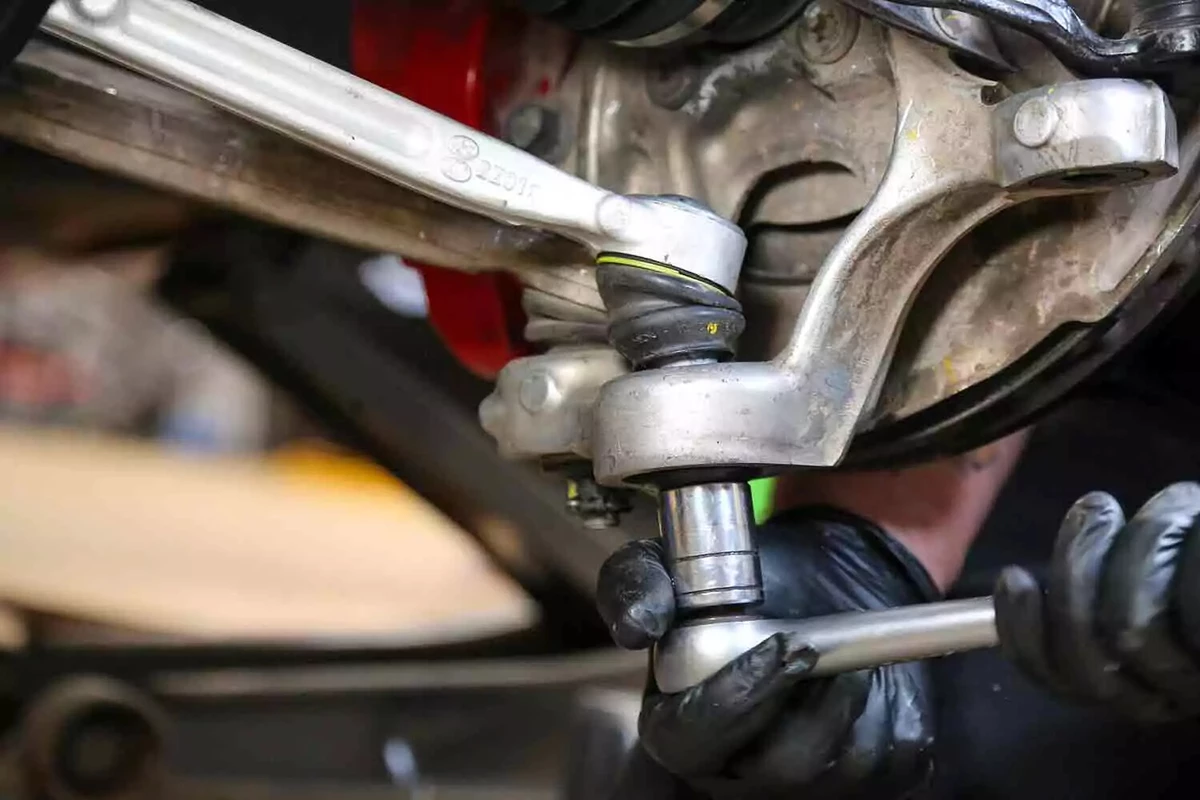 A mechanic wearing black nitrile gloves uses a socket wrench to disconnect the suspension from the wheel hub.