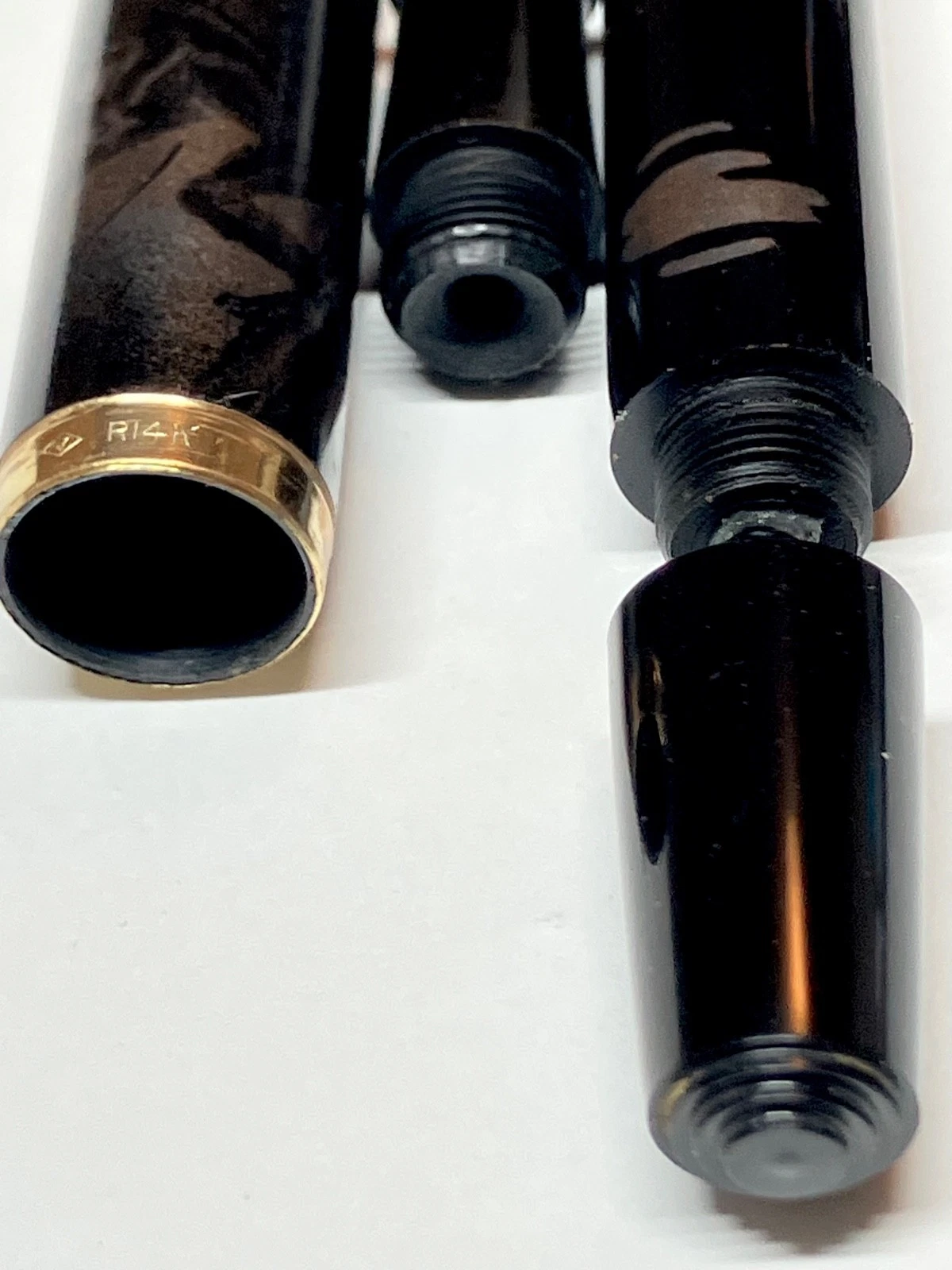 Black vintage fountain pen with gold nib, labeled “R14k,” beside brown ink shut off fountain pen with gold accents.